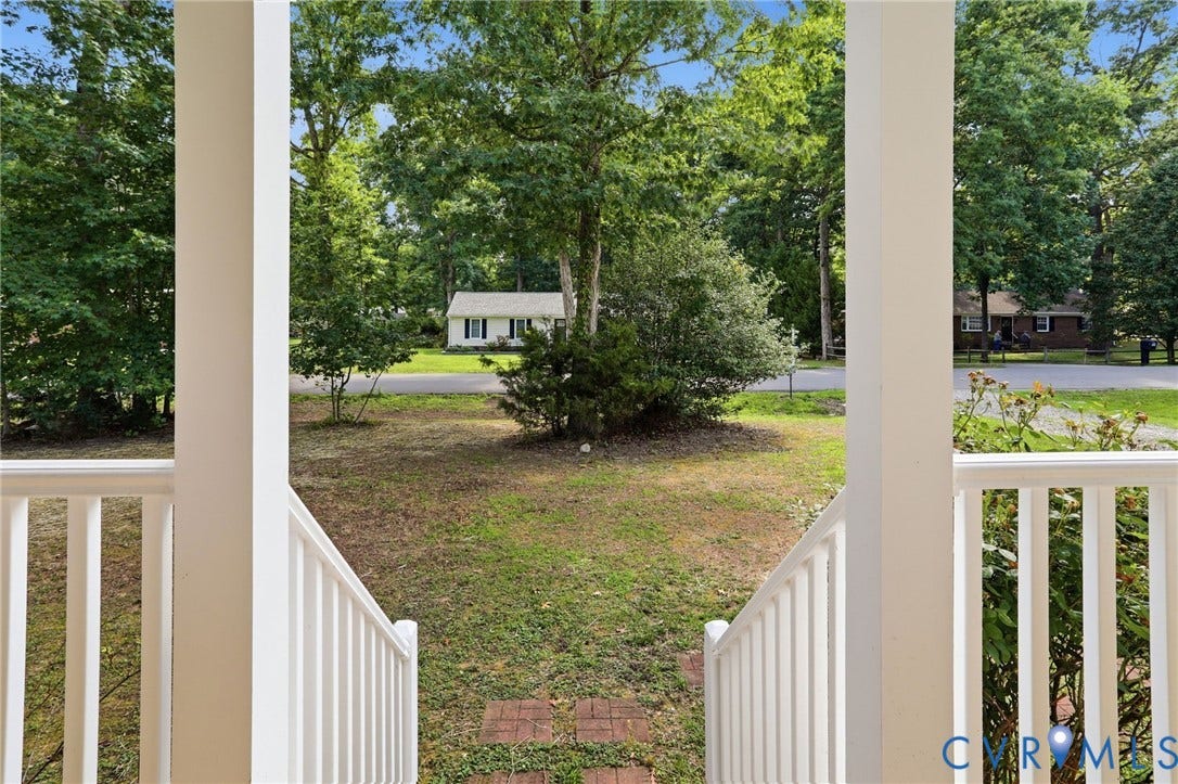 Inviting porch with white railings and columns, providing a framed view of the expansive front yard