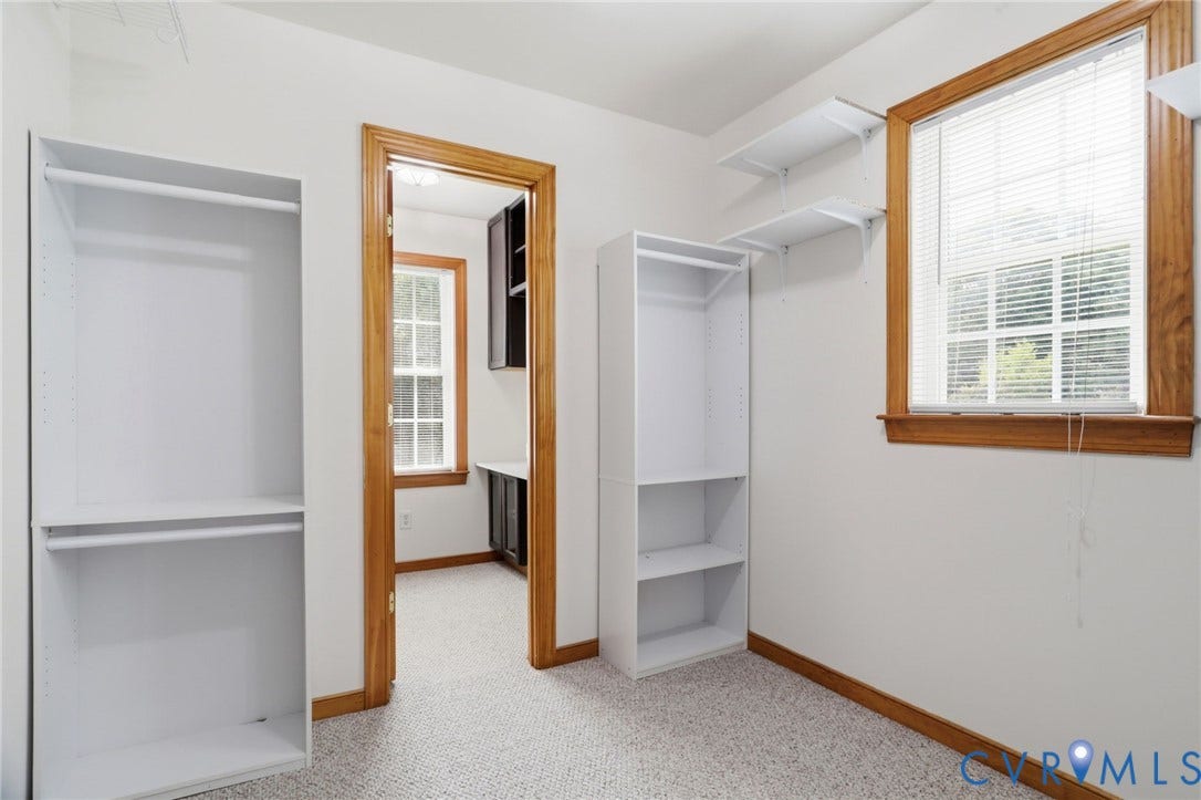 Room featuring light-colored carpet flooring, white walls, and wood-trimmed windows