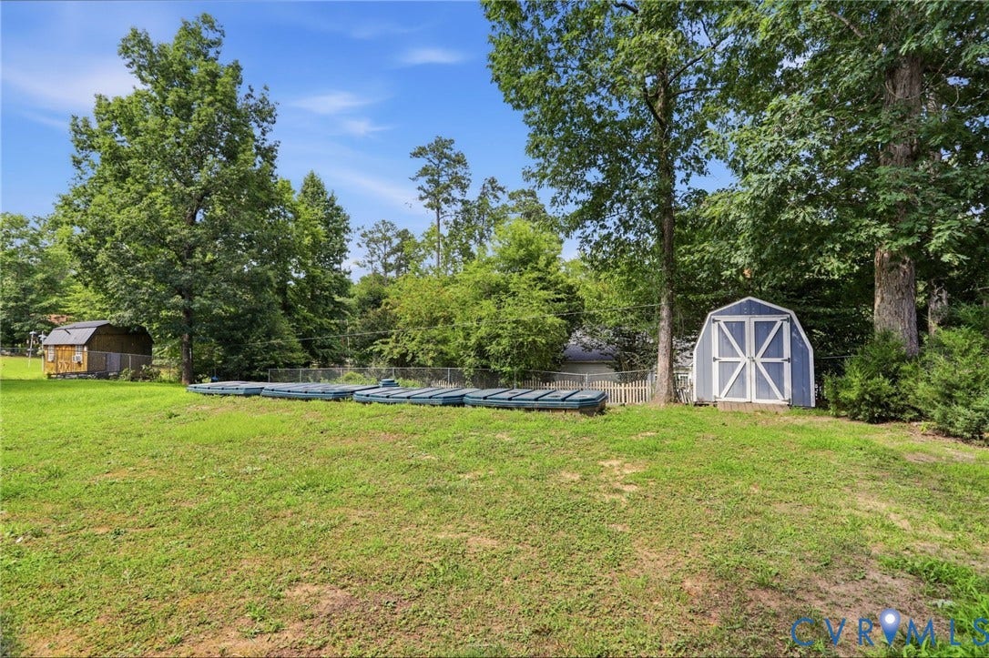 Expansive backyard featuring a manicured lawn, a blue and white storage shed, and a wooden accessory building