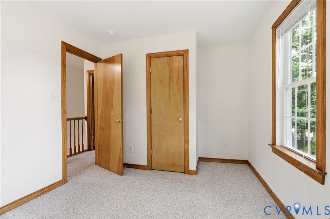 Carpeted room featuring natural wood trim, a single window, and two solid wood doors