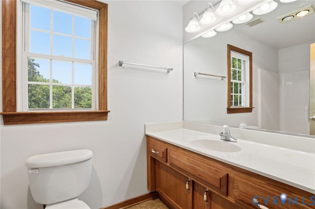 Bathroom featuring a white toilet, a window with wood trim, a wood-finish vanity with a white countertop, and an integrated sink with a chrome faucet
