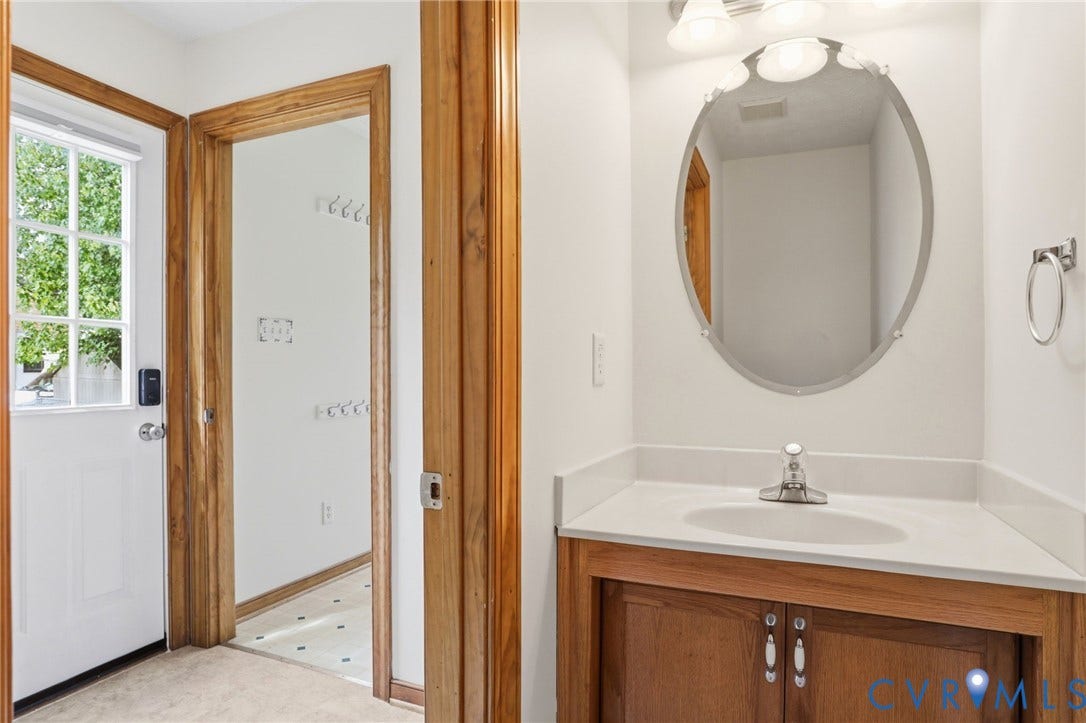Corner vanity with a white countertop and integrated sink, complemented by a wood-finish cabinet and an oval mirror