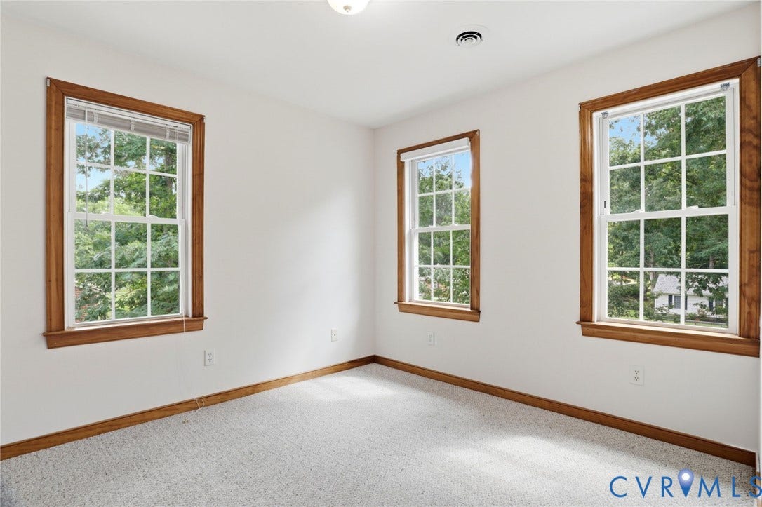 Room featuring light-colored carpeting, white walls, and three windows with wooden trim