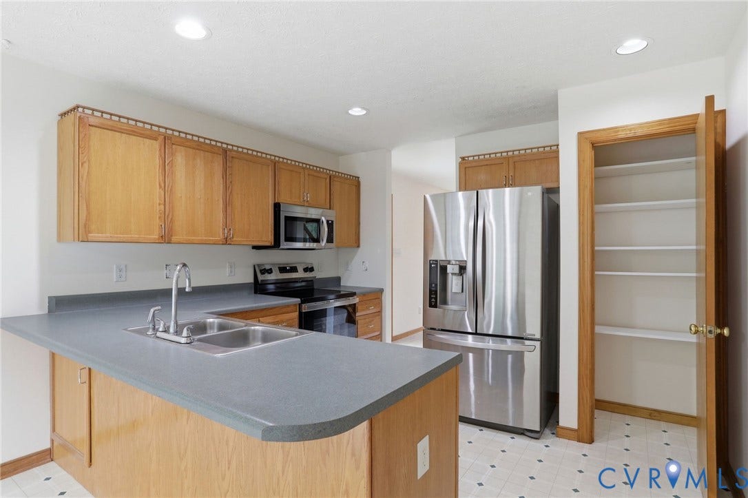 Kitchen featuring light wood cabinetry, stainless steel appliances, a double basin sink, recessed lighting, and an organized pantry with shelving