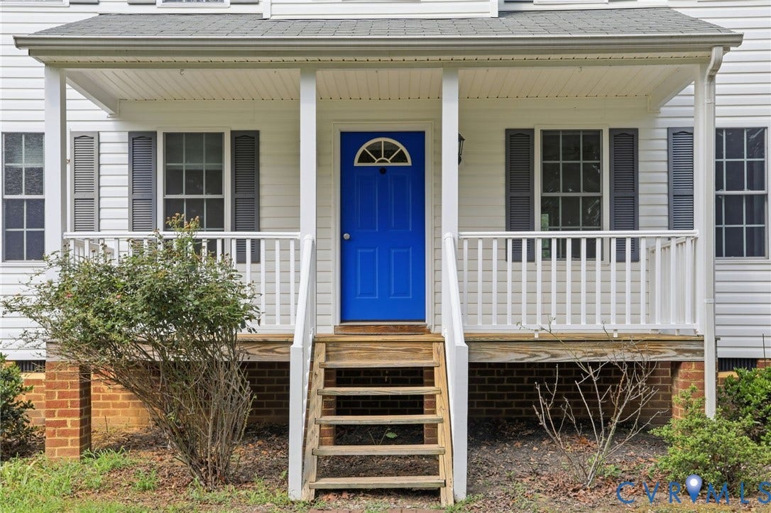 Welcoming covered front porch featuring white siding, a vibrant blue entry door with an arched transom, and dark grey louvered shutters