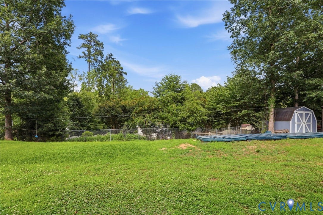 Expansive lawn area featuring a chain-link fence, mature trees, and a storage shed with a white trim