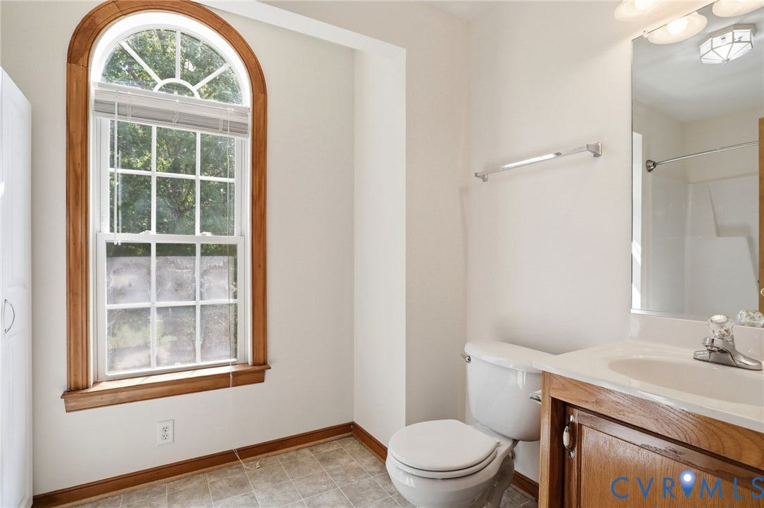 Arch-top window with wood trim, white vanity with integrated sink, wood-finish vanity cabinetry, toilet, and square tile flooring