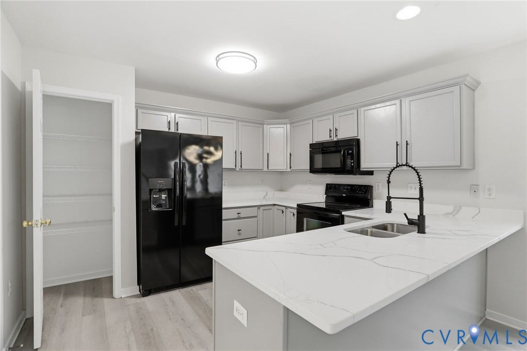 6412 Autumn Mist Way, Chesterfield, VA 23832 Modern kitchen featuring light gray cabinetry, black appliances, light wood-finish flooring, a white countertop island with an undermount sink, and a walk-in pantry with wire shelving