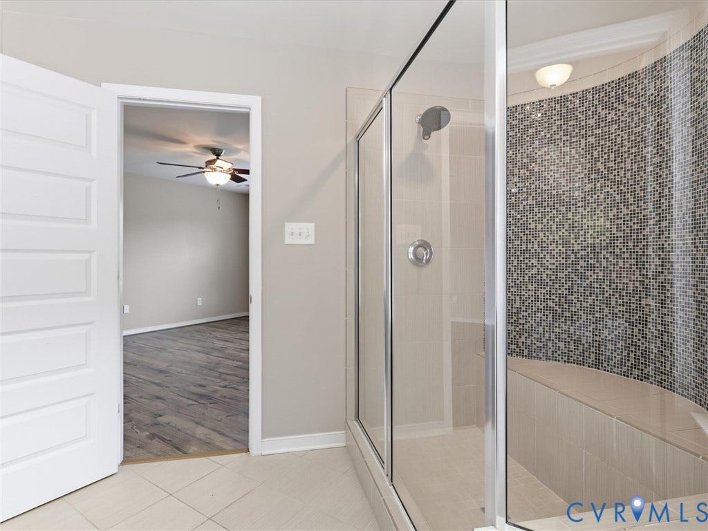 17431 Memorial Tournament Drive, Wynstone Park, Moseley, VA 23120 The spa-inspired primary bathroom boasts an oversized tiled walk-in shower with sleek glass enclosure, a built-in bench with striking mosaic tile accents, and neutral designer finishes for a timeless, sophisticated look.