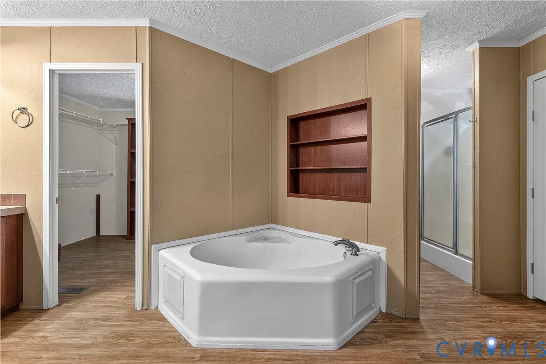 4106 S Spotswood Trail, Trevilians, Louisa, VA 22942 Corner soaking tub with chrome fixtures, integrated wall shelving, wood-finish flooring, and a stand-up shower with a glass enclosure