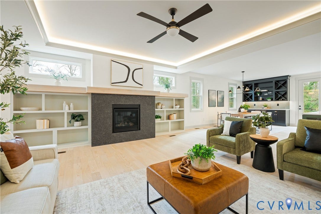 8919 Rustic Road, Richmond, VA 23235 Spacious living area featuring a dark stone-clad fireplace with a natural wood mantel, built-in shelving, light wood-finish flooring, and a tray ceiling with recessed lighting