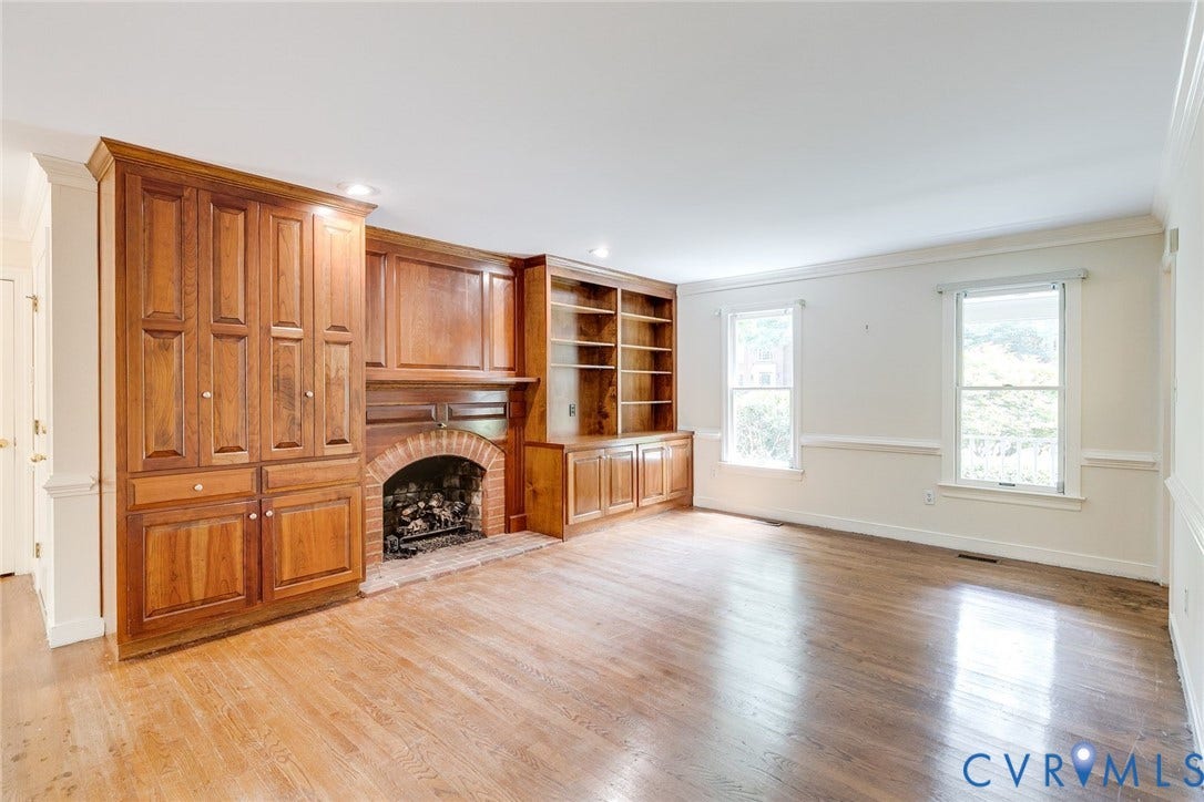 Living area featuring custom built-in cabinetry, an arched brick fireplace, wood-finish flooring, two large windows, and recessed lighting