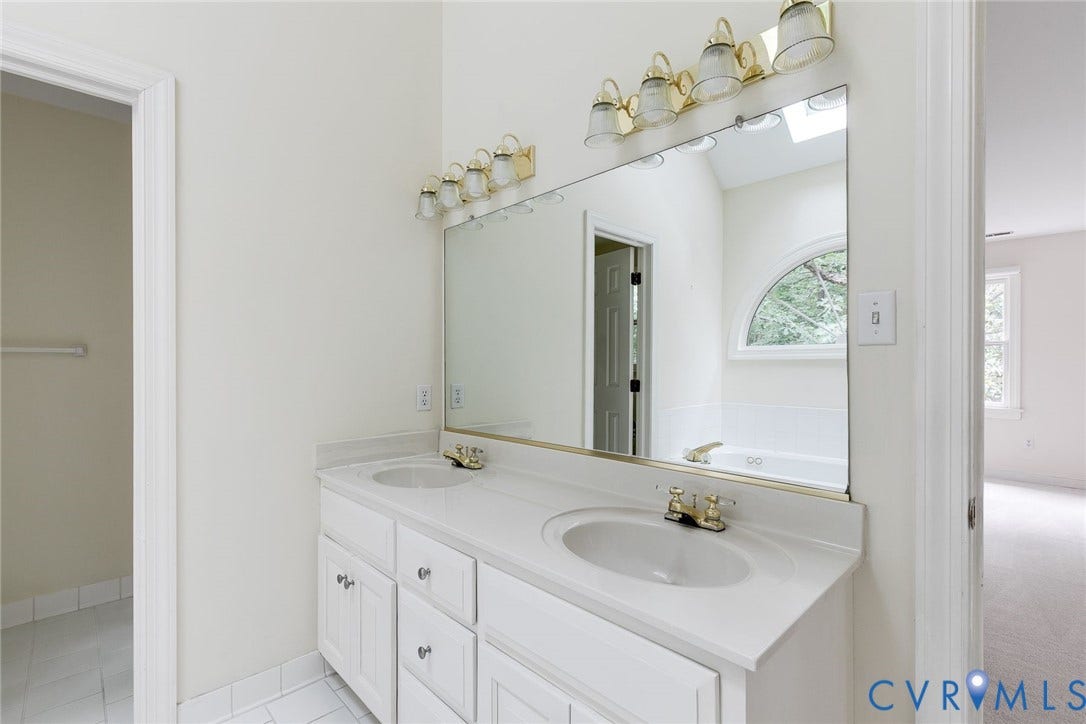 Dual vanity with white cabinetry, integrated sinks, a large wall-mounted mirror, and brass-finish lighting fixtures