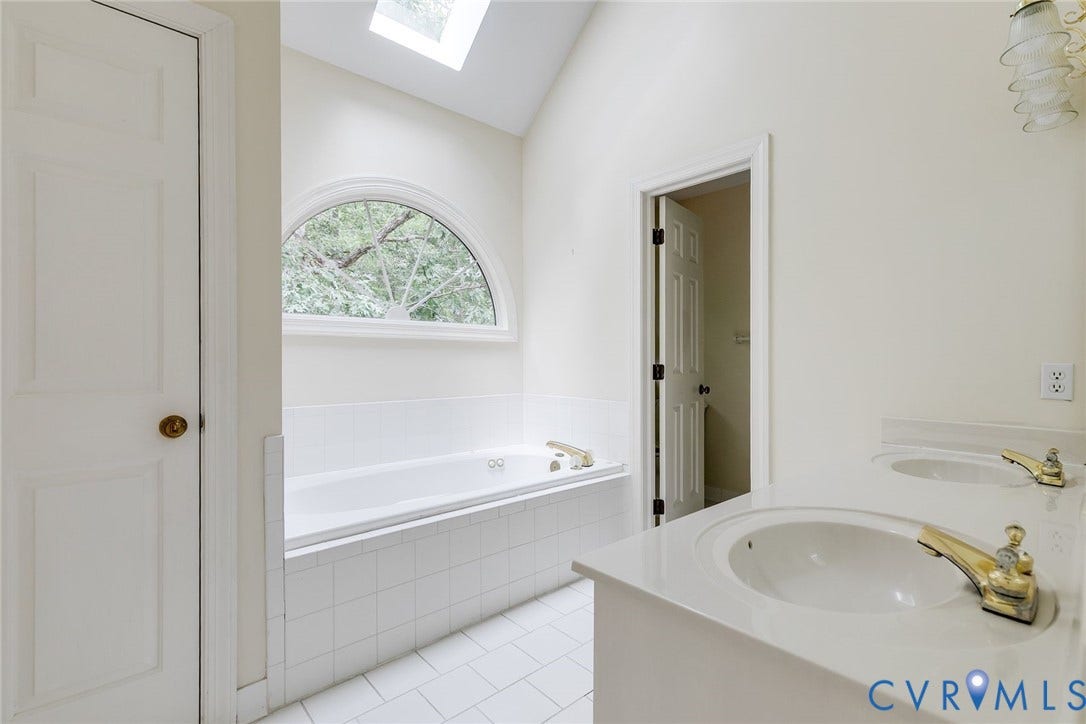 Bathroom featuring a soaking tub with an arched window, a skylight, and a double vanity with integrated sinks