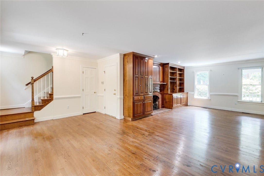 Spacious interior featuring wood-finish flooring, a built-in fireplace with brick surround, extensive built-in cabinetry and shelving, and a prominent staircase with wood railing