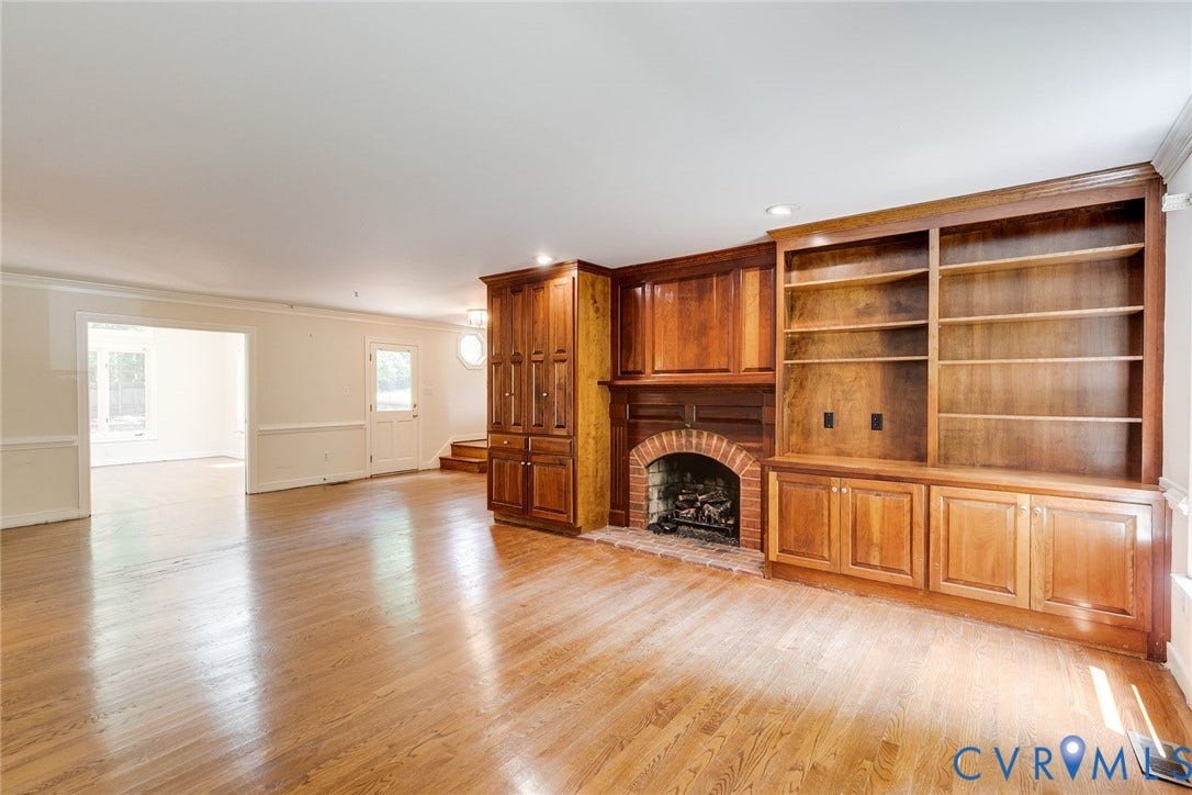Living area featuring hardwood flooring, a brick fireplace, built-in wooden cabinetry, and shelving