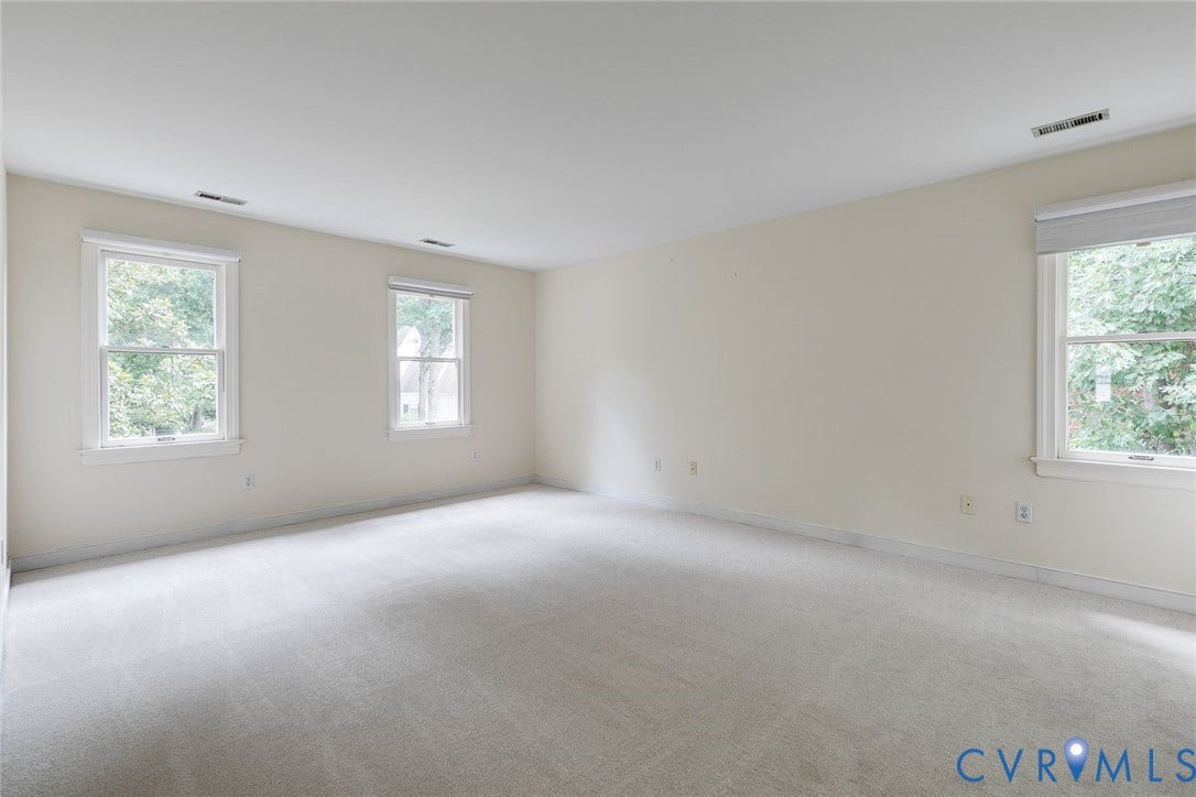 Spacious room featuring light-colored walls and soft gray carpeting