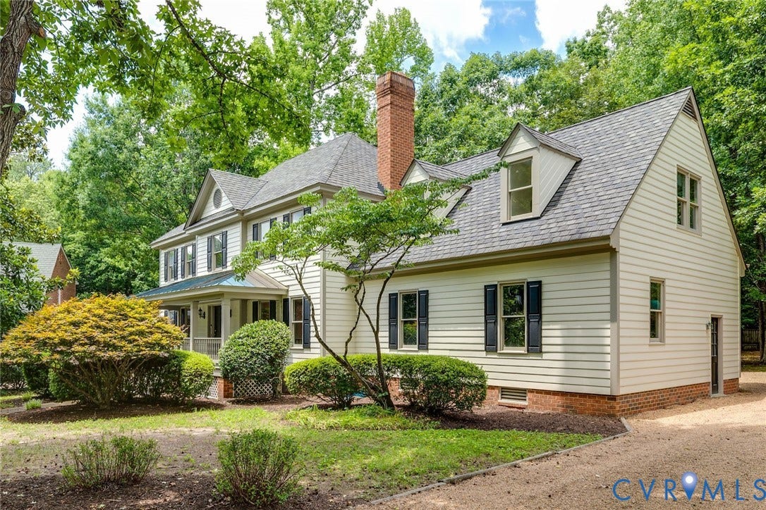 Colonial-style residence featuring light-toned siding, dark shutters, and a prominent brick chimney