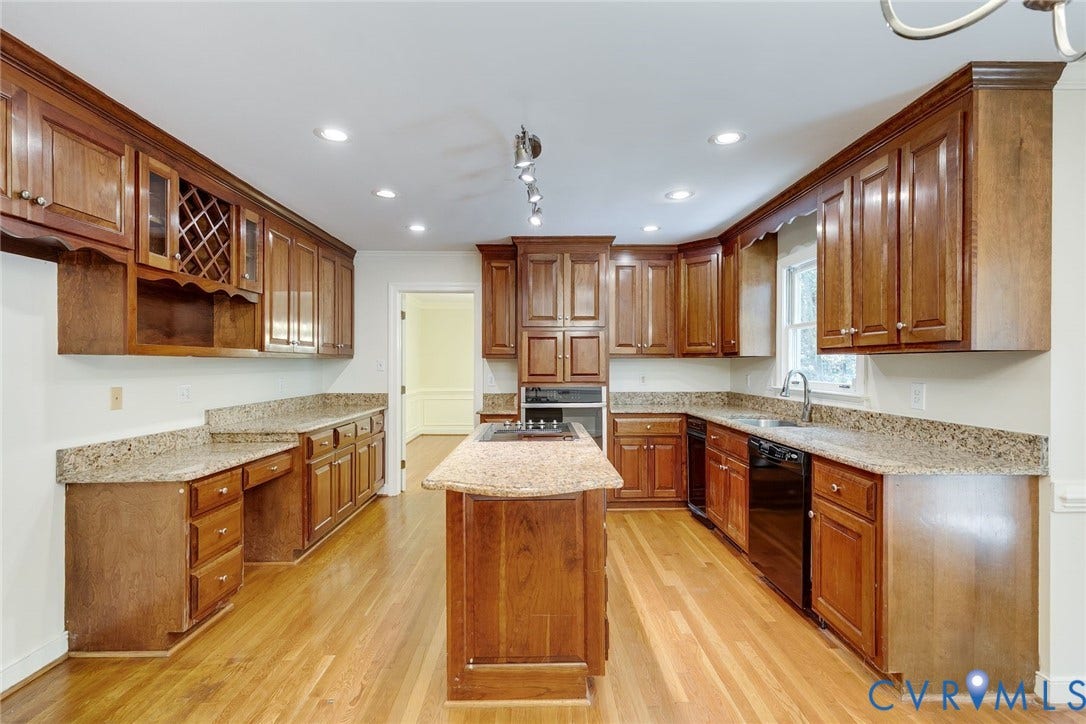 Kitchen featuring wood-finish flooring, an island with cooktop, black appliances, and extensive wood cabinetry with granite-style countertops