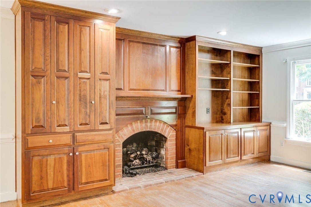 Built-in cabinetry featuring a brick arch fireplace, recessed lighting, wood-finish flooring, and a large window