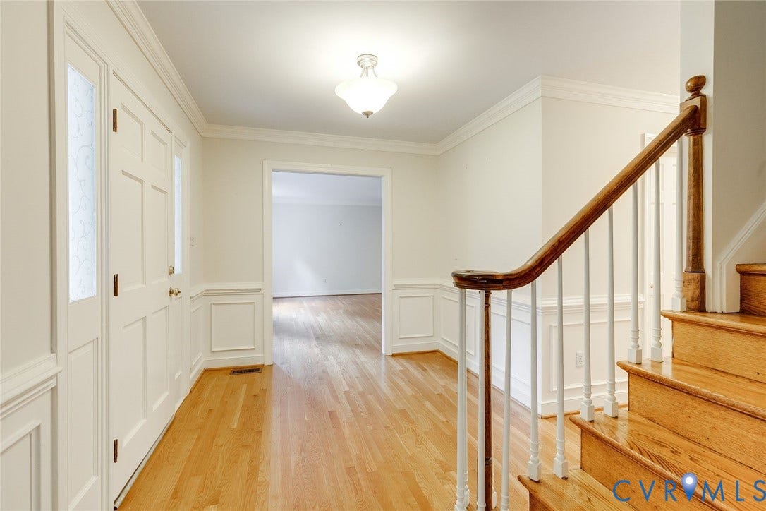 Hardwood flooring extends throughout the entryway, featuring a solid panel front door with a decorative glass sidelight