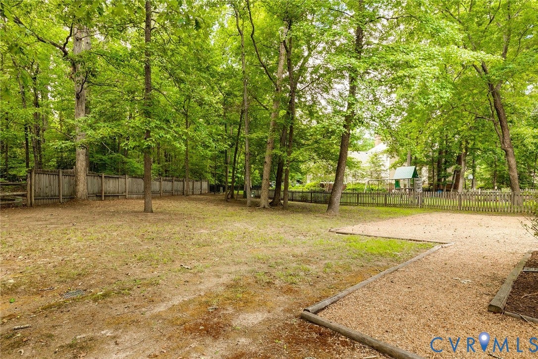 Expansive rear yard featuring mature trees, a wood privacy fence, and a wood chip surface area
