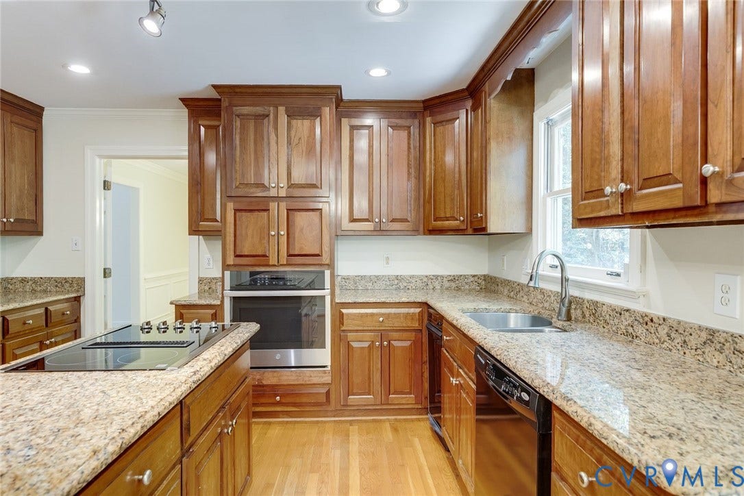 Kitchen featuring abundant wood cabinetry, granite countertops, wood-finish flooring, stainless steel appliances, and a built-in cooktop