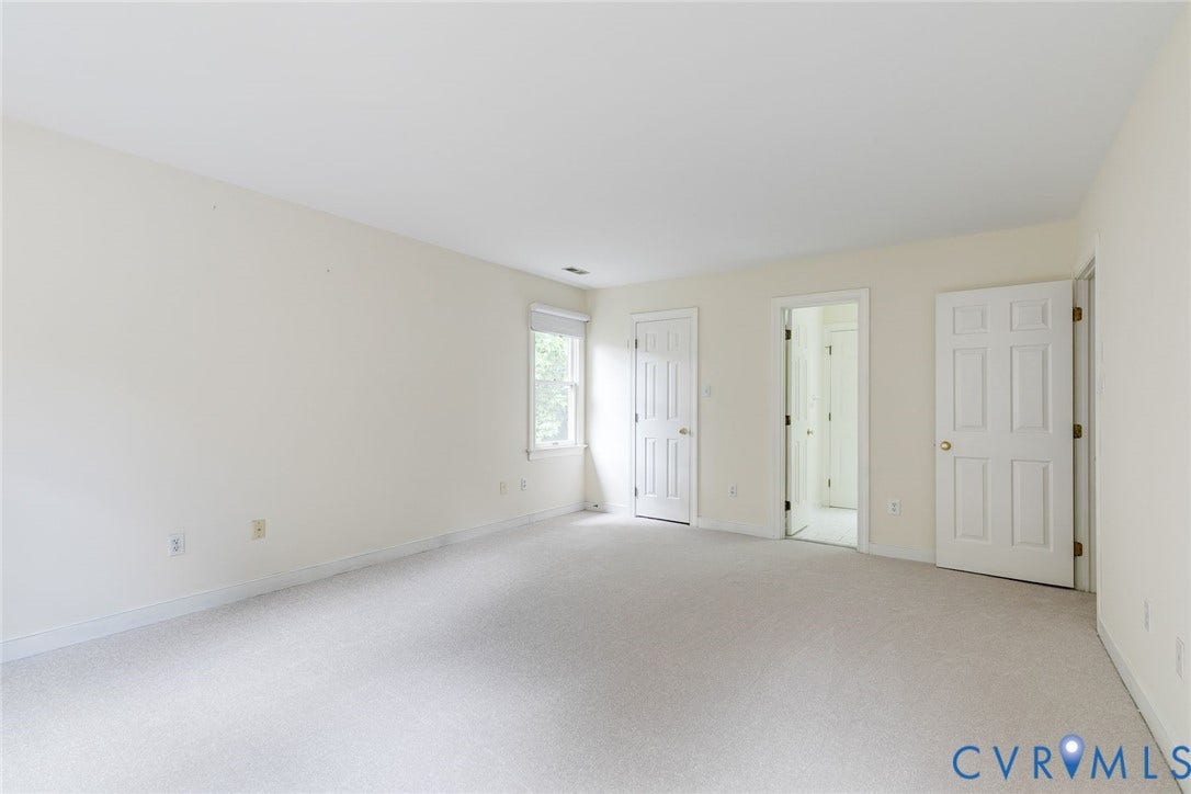 Spacious room featuring light-colored carpeting, neutral wall tones, and multiple white paneled doors