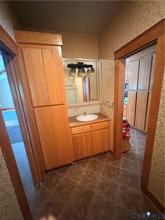 Bathroom featuring a single vanity with an oval sink, natural wood-finish cabinetry, and a large mirror