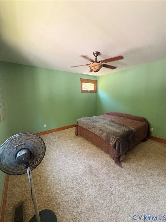Carpeted room with a ceiling fan light fixture, light green wall finishes, and wood trim