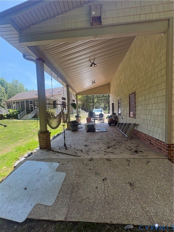 Expansive covered patio featuring a concrete surface, shingle siding, brick foundation, and recessed lighting