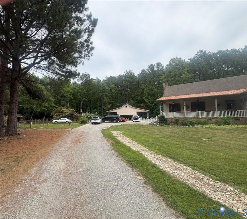 Gravel driveway leading to a residence with a covered front porch and an additional detached building