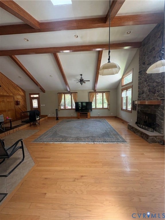 Spacious room featuring a vaulted ceiling with exposed wood beams and a large skylight