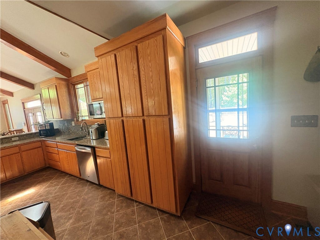Kitchen featuring wood cabinetry, granite countertops, stainless steel appliances, and brown tile flooring