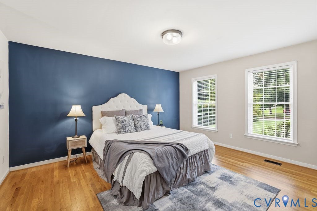 3819 Daniels Street, Chesterfield, VA 23831 Bedroom featuring a prominent accent wall in deep blue, hardwood flooring, two large windows with white blinds, and a flush-mount ceiling light fixture