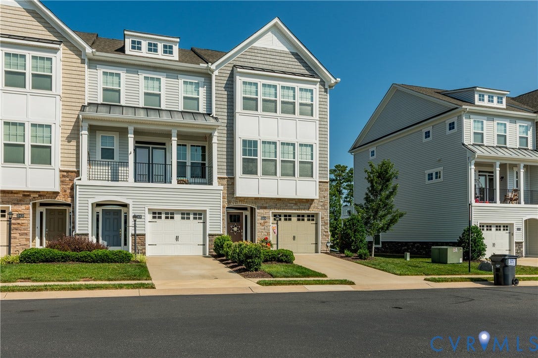 10414 Perennial Drive, Henrico, VA 23233 Multilevel townhome featuring a two-car garage, stone and siding exterior, a second-story balcony with iron railing, and a gabled roofline with a dormer