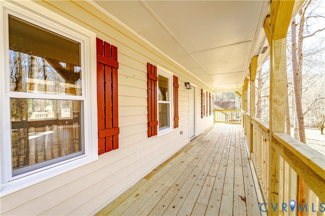 3025 Maplevale Road, Chester, VA 23831 Expansive covered porch featuring natural wood decking and railings, beige siding, white window frames, and decorative red shutters