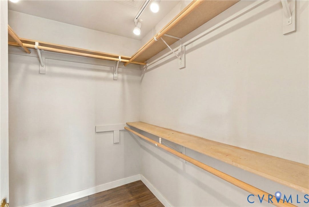 Walk-in closet featuring light wood-finish shelving and hanging rods, track lighting, and wood-finish flooring