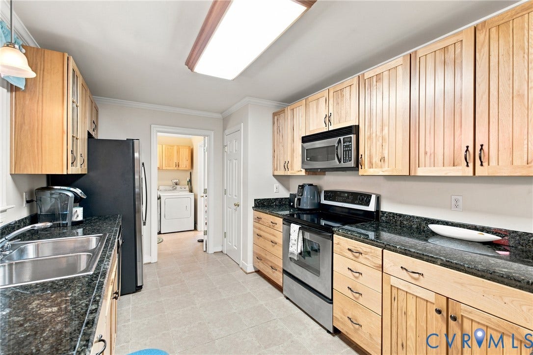 Kitchen featuring light wood cabinetry, dark granite countertops, stainless steel appliances, and tile flooring