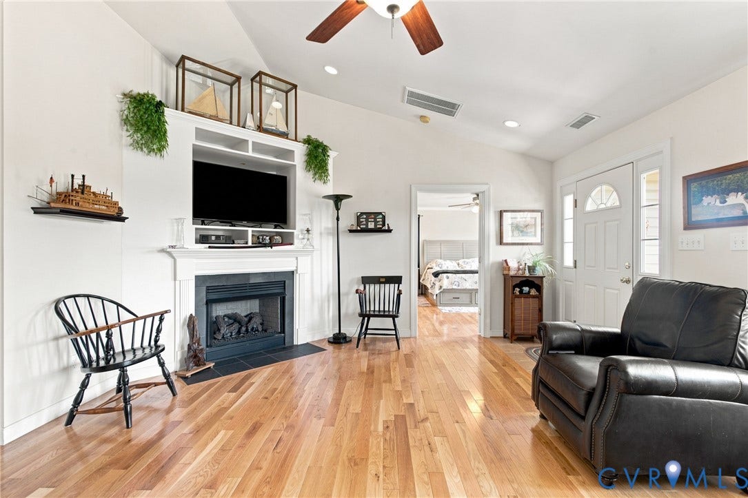 Living area featuring wood-finish flooring, a white mantel fireplace with a black tile hearth, and an entertainment center with shelving