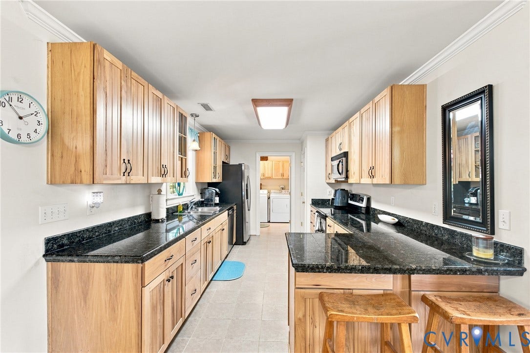 Galley kitchen featuring light wood cabinetry, dark granite countertops, stainless steel appliances, a built-in microwave, and tile flooring