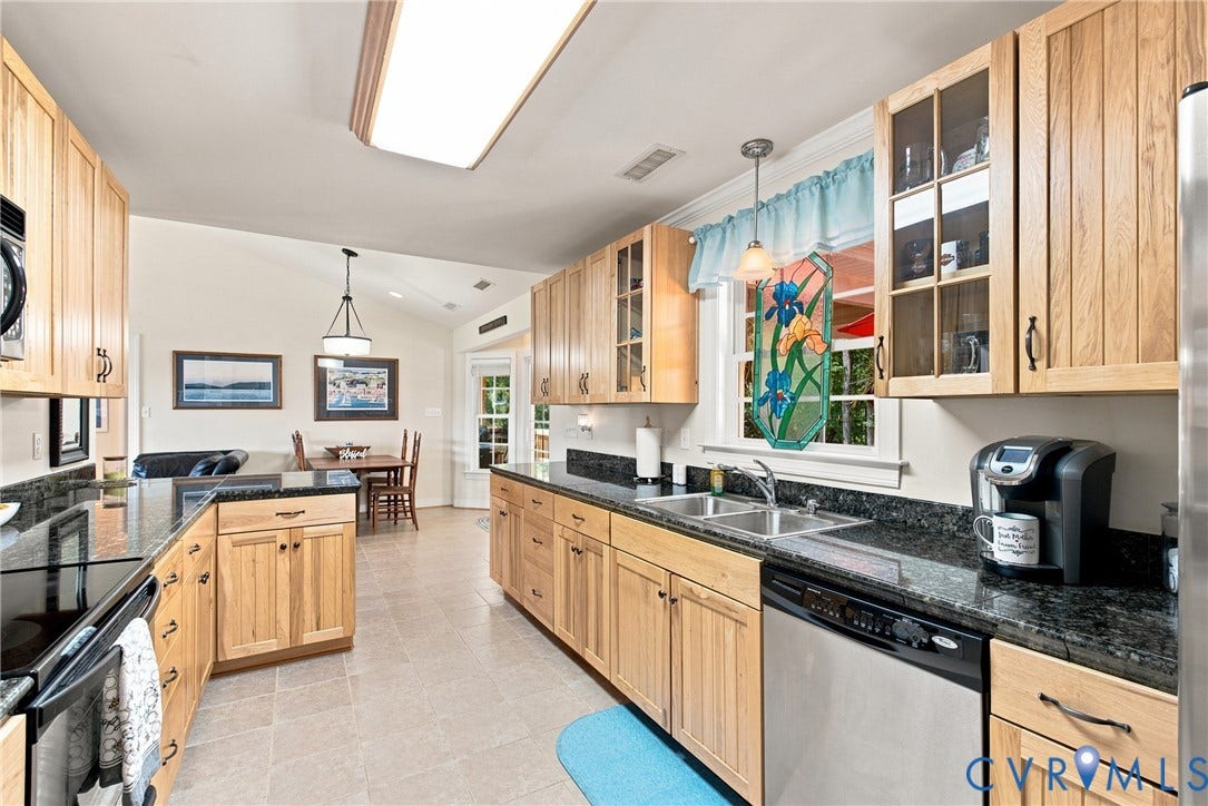 Open-concept kitchen featuring wood cabinetry, dark granite-finish countertops, stainless steel appliances, and tile flooring