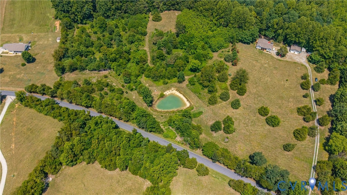 Expansive property featuring a private pond, mature trees, open land, paved road frontage, and a defined gravel driveway