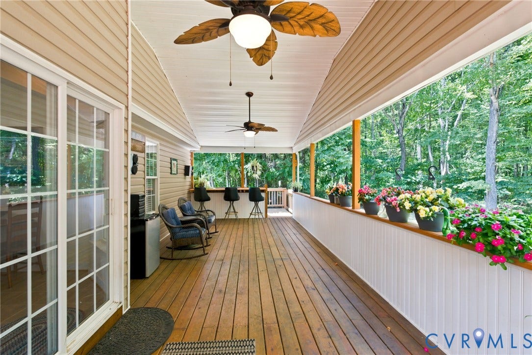 Expansive covered deck featuring wood-finish flooring, two ceiling fans, and a partial privacy wall