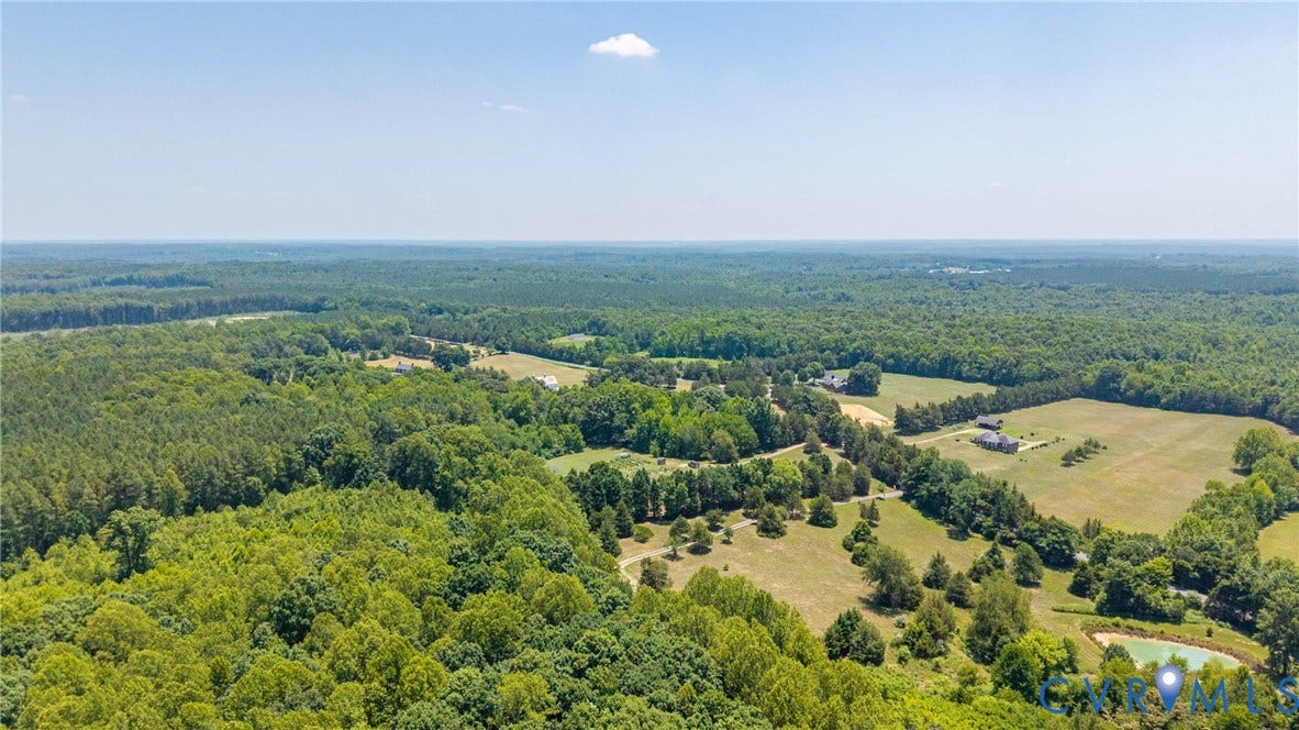 Expansive wooded acreage featuring open fields, scattered structures, and a pond