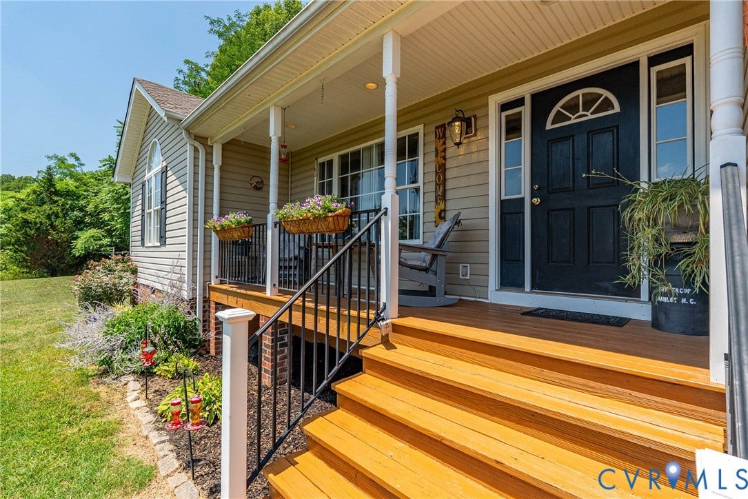 Inviting front porch featuring a black paneled door with an arched transom window, wood-finish steps, white columns, black railings, and a meticulously maintained landscape with mature shrubs