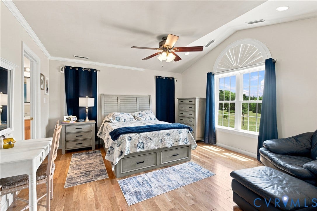 Bright bedroom featuring light wood-finish flooring, a vaulted ceiling, and an arched window with louvered details