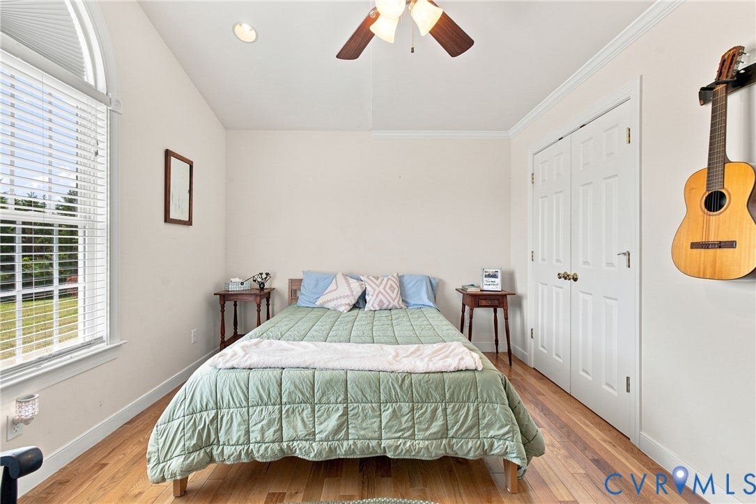 Room featuring a vaulted ceiling with a ceiling fan, wood-finish flooring, and a large window with blinds
