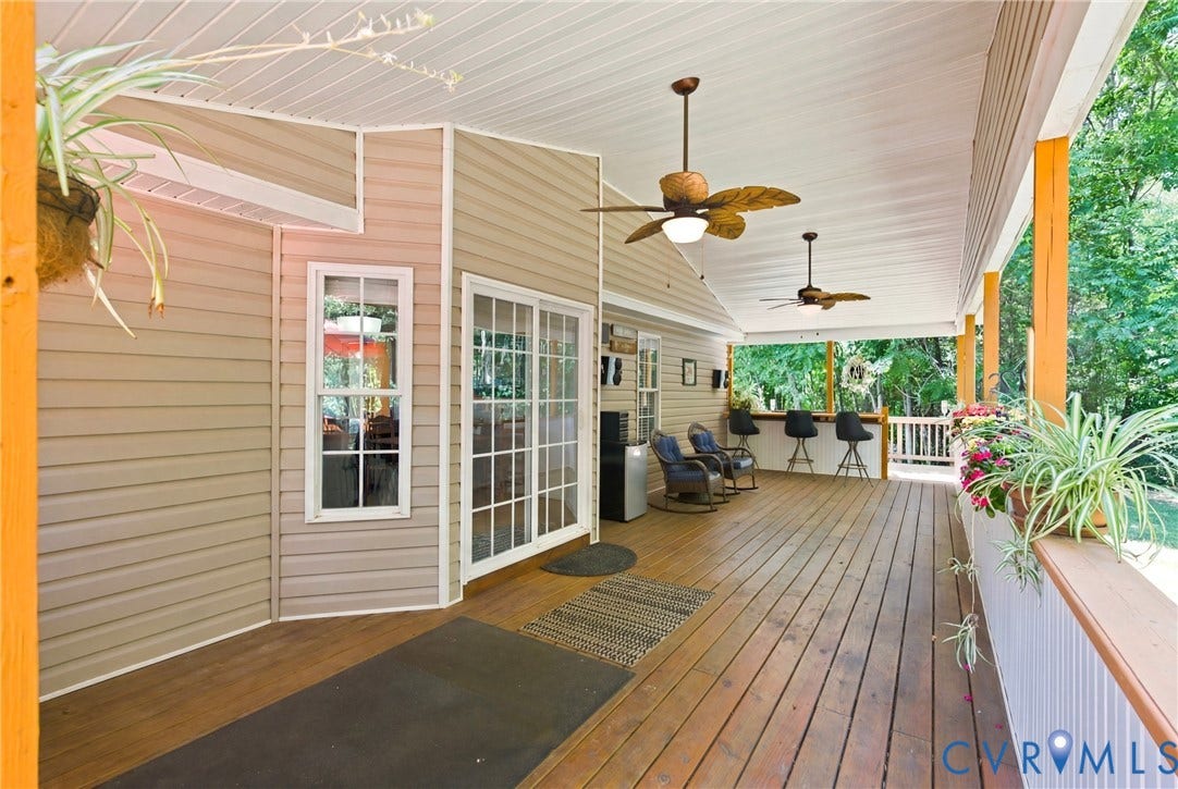 Expansive covered deck featuring wood-finish flooring, two ceiling fans, and a built-in bar