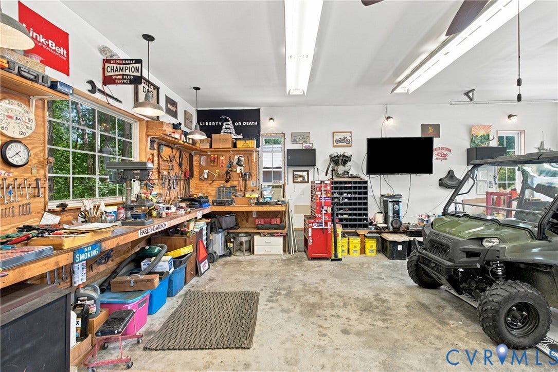 Spacious garage featuring extensive built-in wooden workbench areas, multiple windows providing natural light, and overhead fluorescent lighting